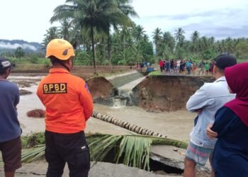 Seorang petugas TRC BPBD Bolmong memantau luapan air sungai akibat cuaca ekstrem hujan lebat. (Foto Dok. BPBD Bolmong)